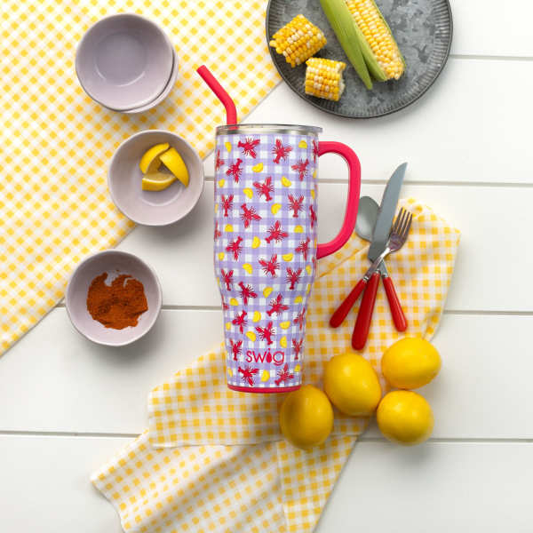 Patterned insulated tumbler with straw surrounded by lemons and picnic dishes