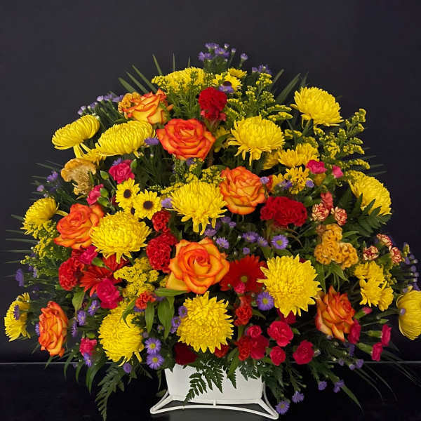 Large mixed flower arrangement in a white vase with yellow, orange, red, and purple blooms