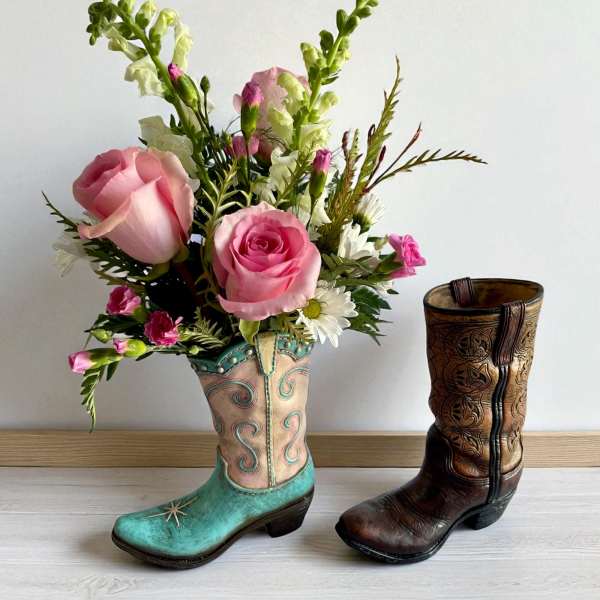 Pink rose bouquet arranged in a turquoise cowboy boot vase beside a brown boot