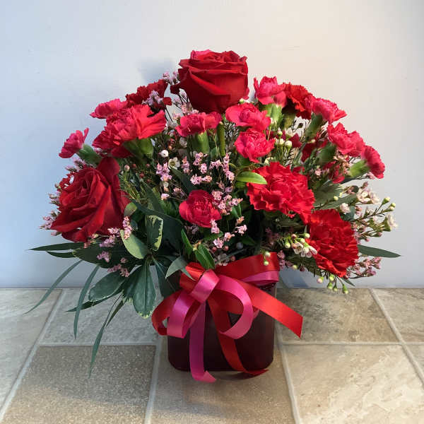 Red roses and carnations in a dark vase with a pink ribbon