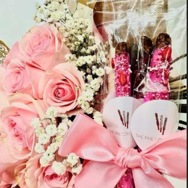 Pink roses with baby's breath and pink gift items tied with a satin bow