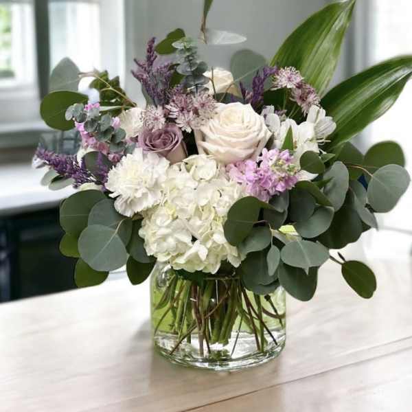 Mixed bouquet of white, blush, and purple flowers in a glass vase