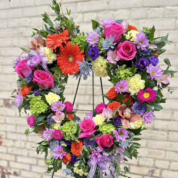 Heart-shaped floral wreath with pink roses and purple daisies on a stand