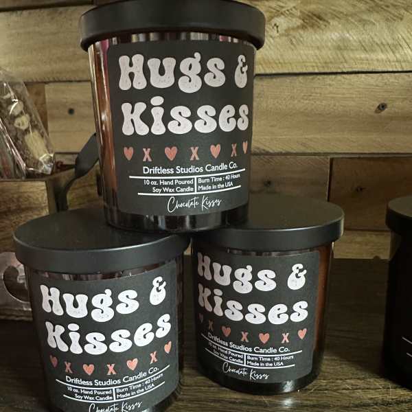 Three black candles labeled "Hugs & Kisses" on a wooden shelf.