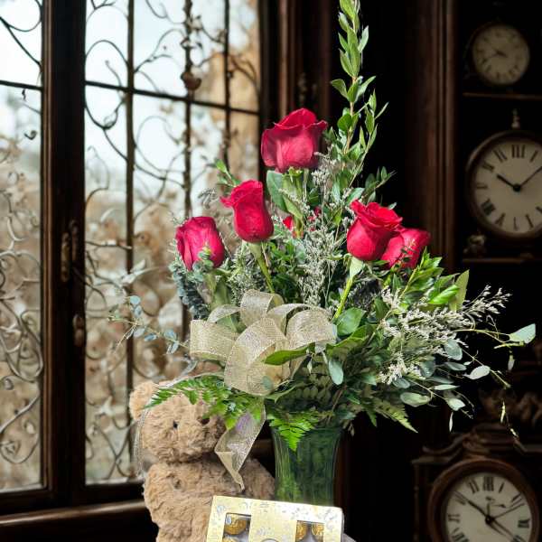 Red roses in a glass vase with a teddy bear and chocolate box