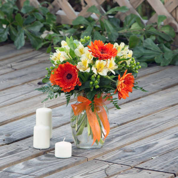 Orange gerbera daisies and white alstroemeria in a glass vase with an orange ribbon