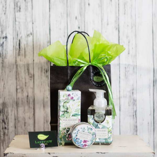 Gift bag with floral-patterned soap and lotion bottles and a small tin