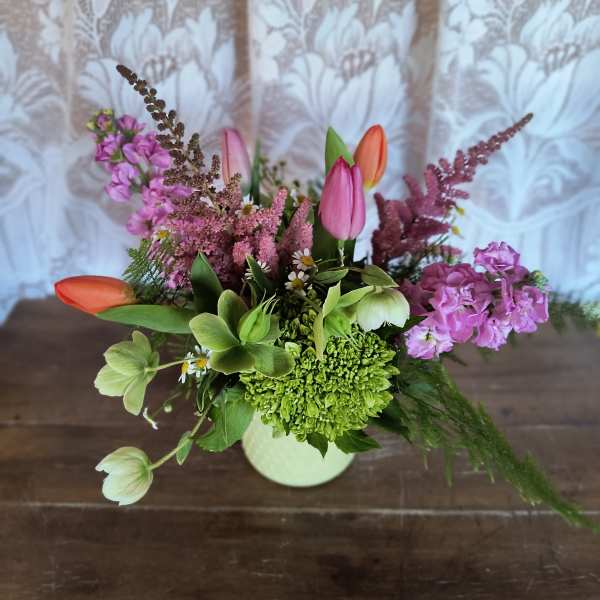 Mixed spring arrangement with pink and orange tulips and green hydrangea in a pale vase
