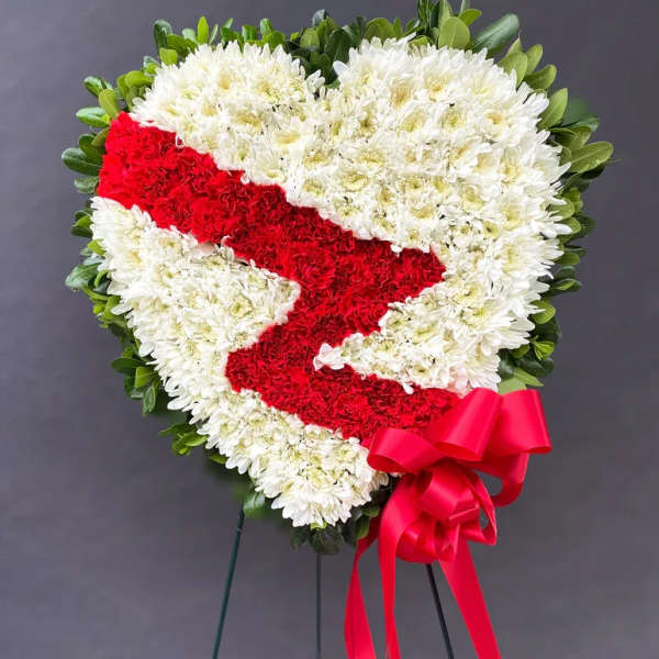 Heart-shaped floral wreath with red ribbon on a stand
