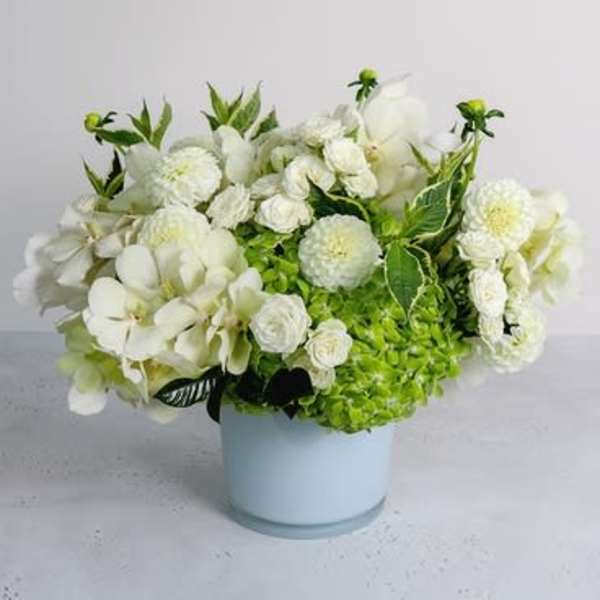 White floral arrangement in a pale blue vase with green accents
