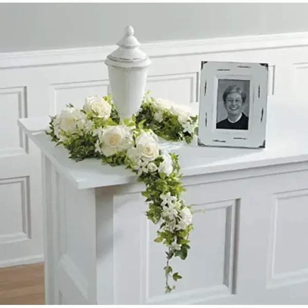 White floral casket spray with a trailing greenery garland and urn centerpiece