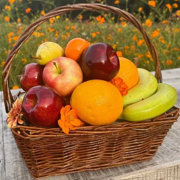 Wicker basket filled with assorted fresh fruits and a few orange blossoms on a rustic wooden surface