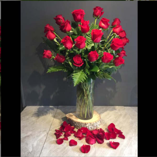 Tall bouquet of red roses in a clear glass vase with rose petals below
