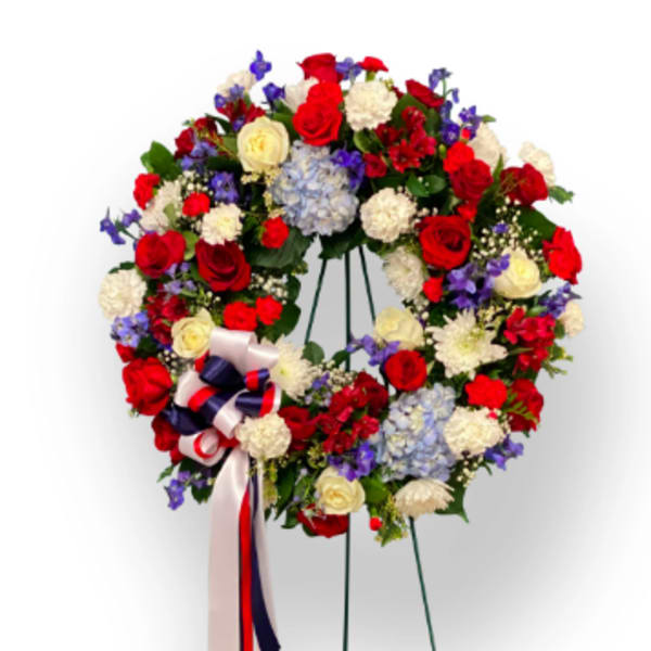 Large floral wreath with red, white, blue, and cream flowers on a stand