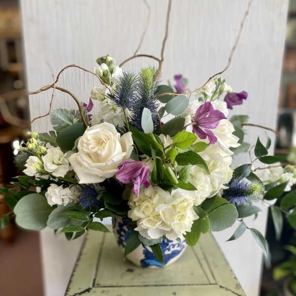 White roses and hydrangeas with purple blooms in a blue-and-white vase