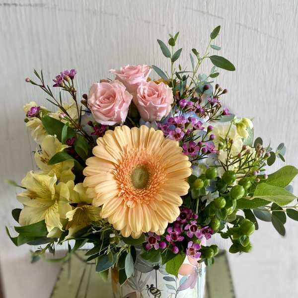 Mixed bouquet with pink roses and a peach gerbera daisy in a floral tin