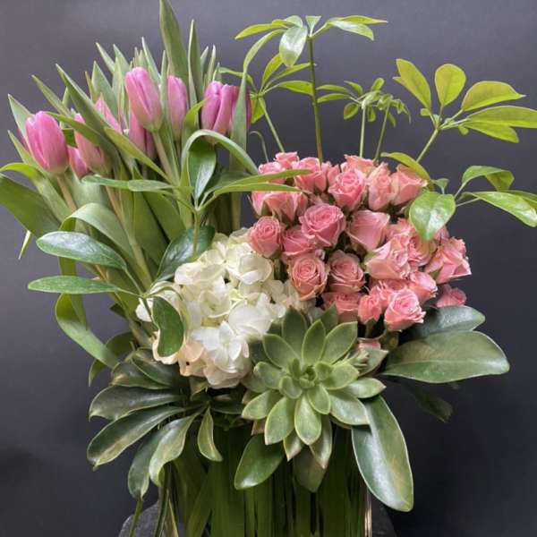 Pink tulips and roses arranged with white hydrangea in a glass vase
