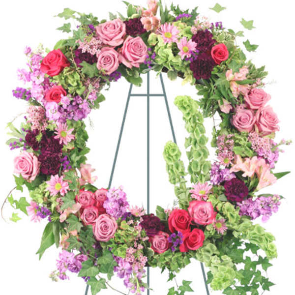 Pink and red rose wreath with purple flowers and green Bells of Ireland on a metal stand