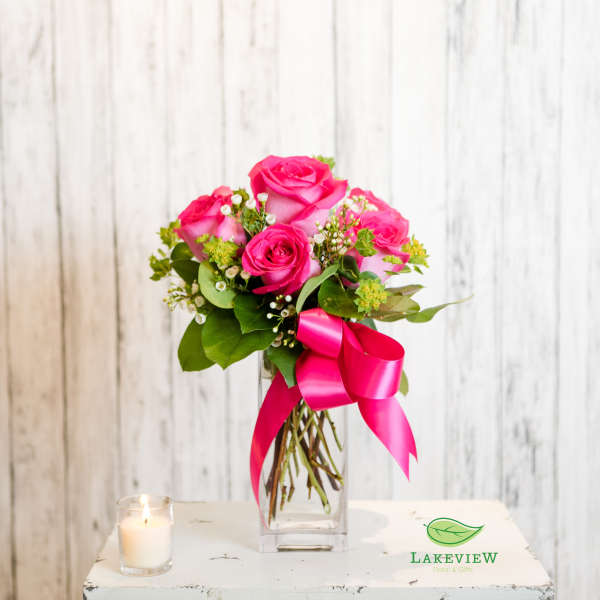 Pink rose bouquet in a clear vase with a bright ribbon and candle