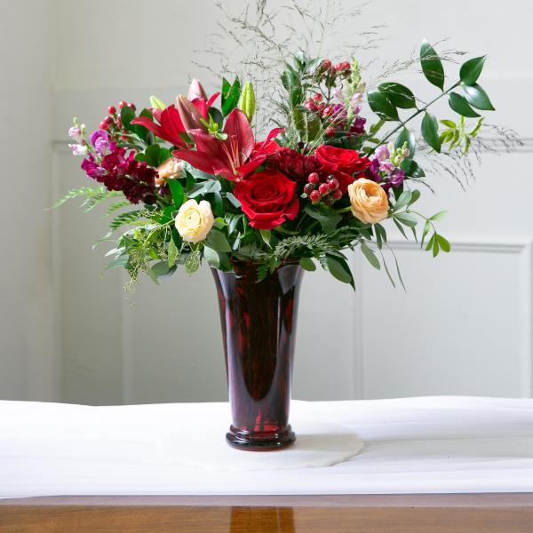 Red roses and lilies arranged in a tall burgundy vase