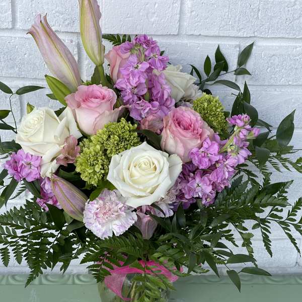 Pink and white roses with lilies and purple blooms in a glass vase