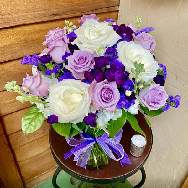 Bouquet of white, lavender, and purple roses in a glass vase with a purple ribbon