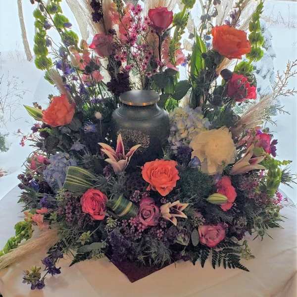 Large floral centerpiece with roses and tall mixed blooms around a black urn