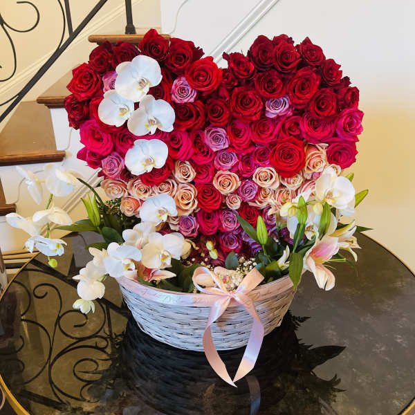 Heart-shaped rose arrangement in a wicker basket with white orchids and lilies
