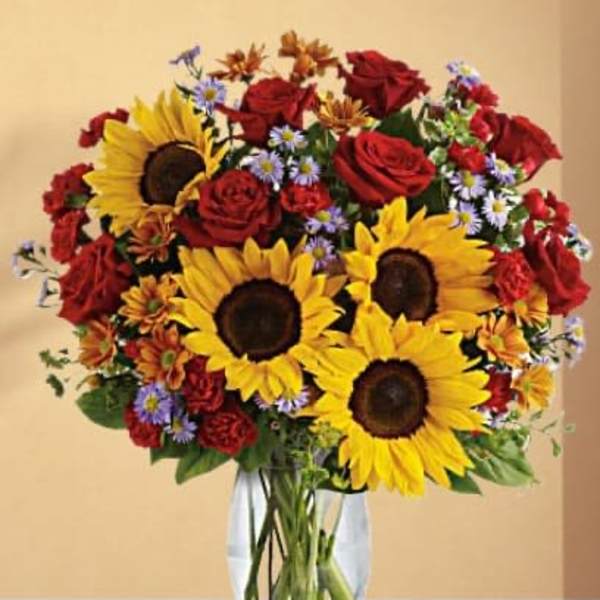 Bouquet of sunflowers, red roses, and small purple daisies in a clear vase