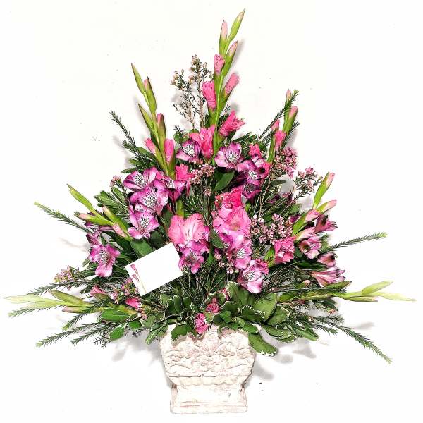 Tall pink floral arrangement in a white urn-style vase with a small card