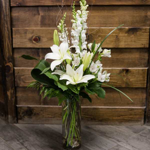 White lilies and snapdragons in a tall glass vase