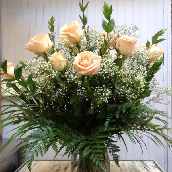 Peach roses in a clear glass vase with baby's breath and greenery