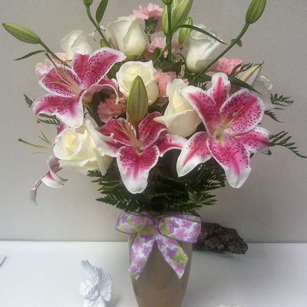 Pink lilies and white roses in a vase with a ribbon bow