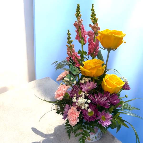 Bouquet of yellow roses, purple daisies, and pink snapdragons in a floral container
