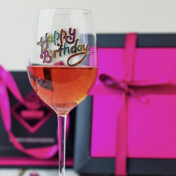 Wine glass with a colorful happy birthday decal, filled with pink drink