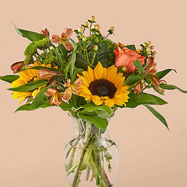 Sunflowers and peach roses arranged in a clear glass vase