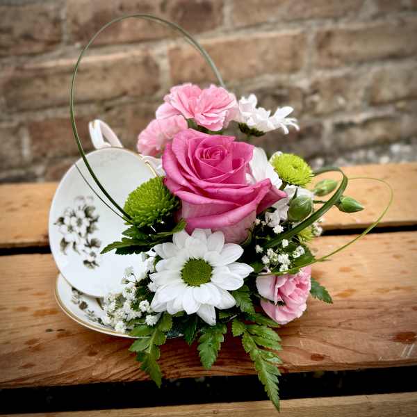 Pink rose and white daisy arrangement in a teacup with a handle