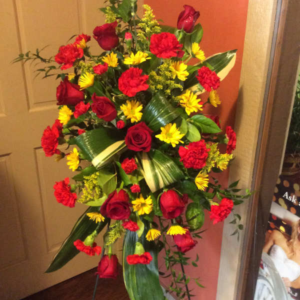 Standing floral spray with red roses, red carnations, and yellow daisies