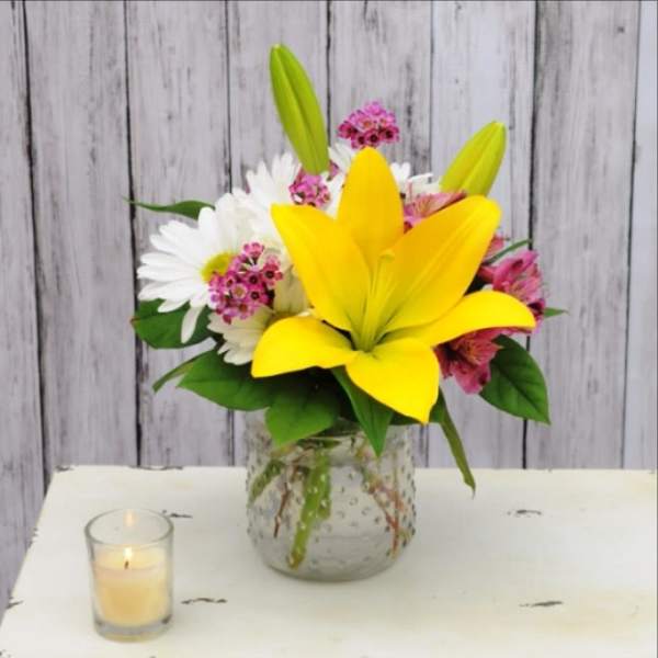 Yellow lily bouquet with white daisies and pink flowers in a glass vase