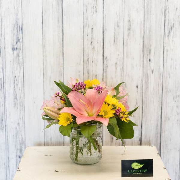 Pink lily and yellow daisy bouquet in a glass jar vase