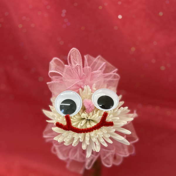 White flower with googly eyes and pink ribbon on a red background