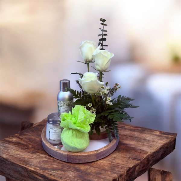White roses in a small arrangement with candles and a green wrapped gift