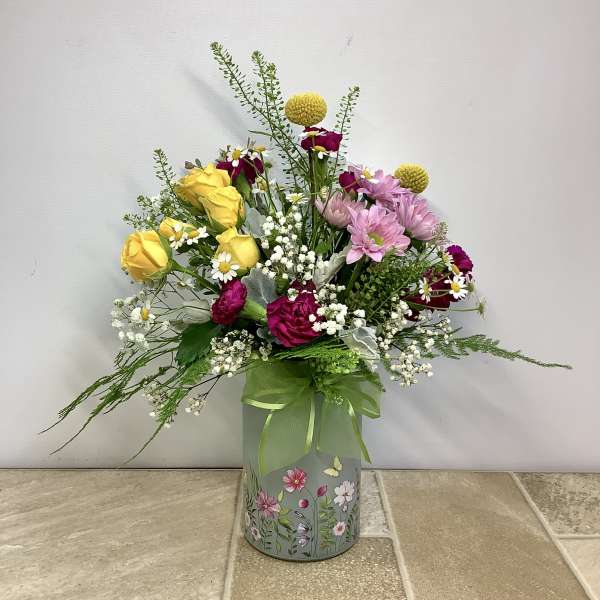 Mixed bouquet of yellow roses and pink flowers in a decorated tin container