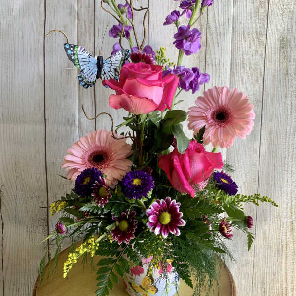 Pink roses and gerbera daisies in a decorated vase with a butterfly accent