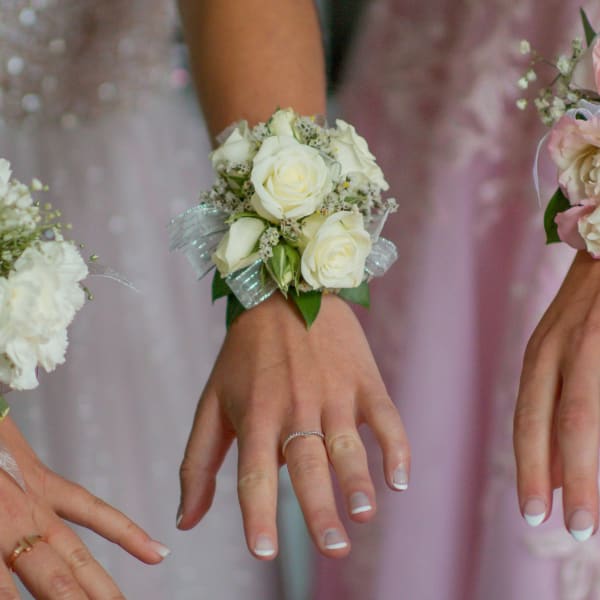 White rose wrist corsage on a hand with ribbon accents
