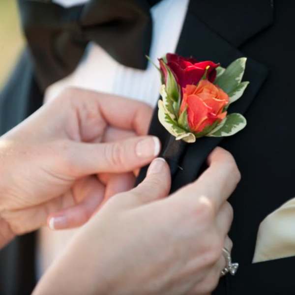 Hands pinning a rose boutonniere onto a tuxedo lapel