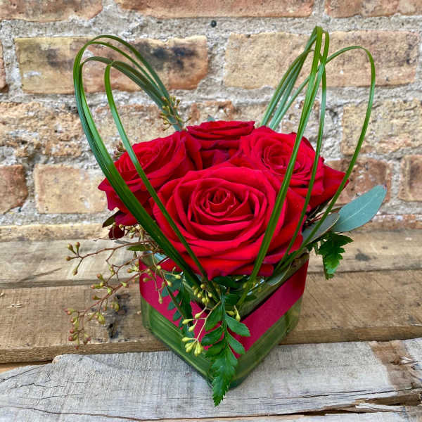 Red roses in a square glass vase with looping grass accents
