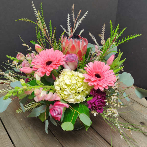 Mixed bouquet with pink gerbera daisies, roses, and a protea in a low vase