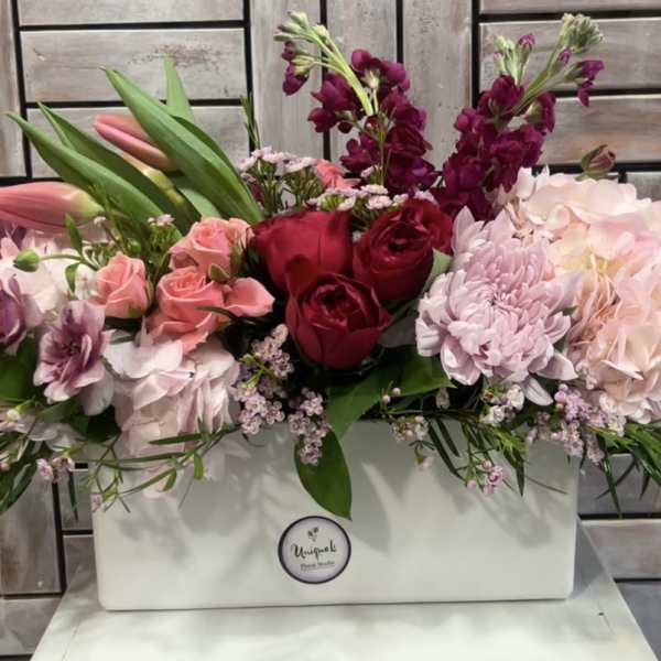 Mixed pink and red flowers arranged in a white rectangular box