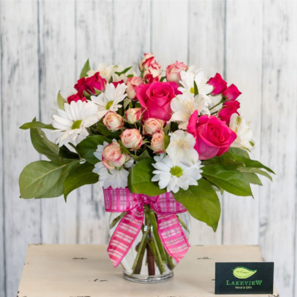 Bouquet of pink roses and white daisies in a glass vase with a pink ribbon